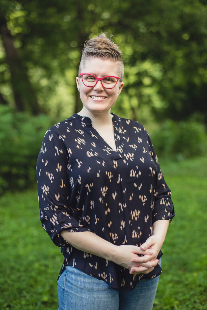 A woman standing in the grass wearing glasses.